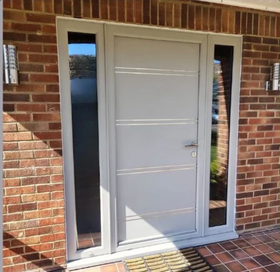 Light grey modern front door with stainless inlays and full length sidelights on red brick home