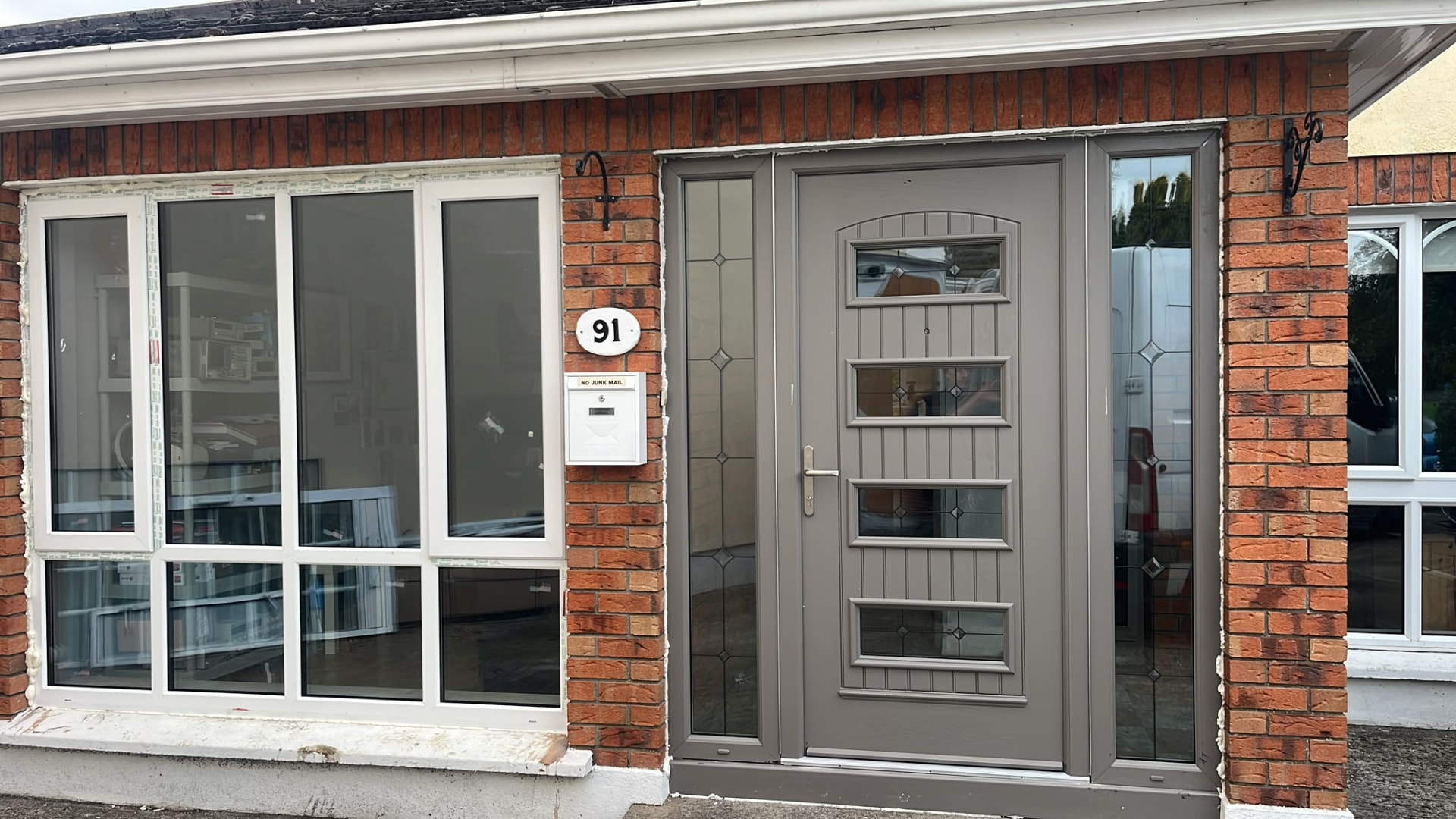Grey composite front door with twin sidelights beside matching white PVC windows